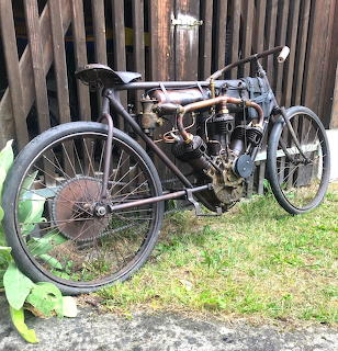 Antique 1903 Buchet 3-cylinder motorcycle with black frame and large spoked wheels on grass