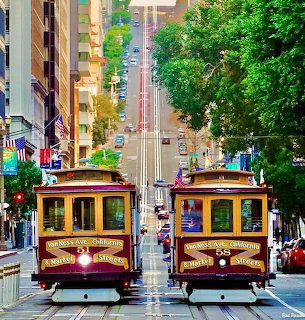 Two cable cars on tracks descending a steep San Francisco street with buildings and greenery on both sides