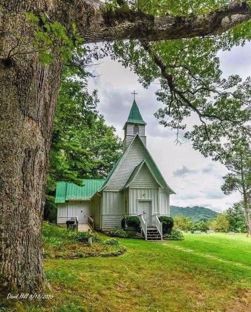 Small white country church with green roof surrounded by trees and green hills