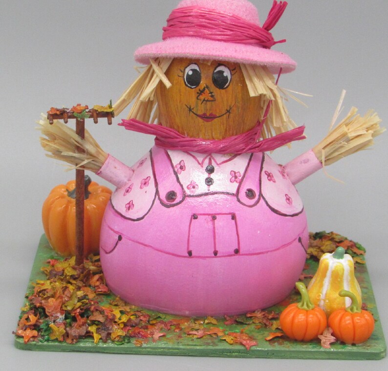 Pink scarecrow cake with straw hat and pumpkins on autumn leaf base