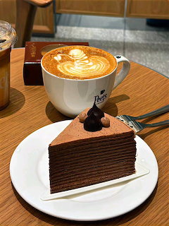 Layered chocolate cake slice with a latte art coffee on a wooden cafe table