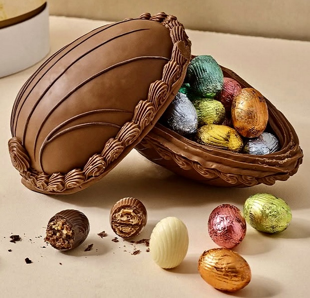 Woven basket with lid containing colorful foil-wrapped chocolate Easter eggs, scattered eggs on surface