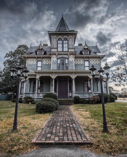 Front view of an ornate Victorian house with a brick path, lawn, and cloudy sky