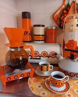 Vintage 1970s orange kitchen items including coffee maker, cups, canisters, and thermos on a counter