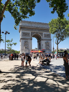 Arc de Triomphe monument in Paris with visitors and trees under blue sky