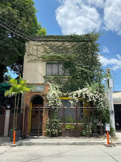 Two-story building covered in green ivy and white flowering vines with a brick entrance and metal fence