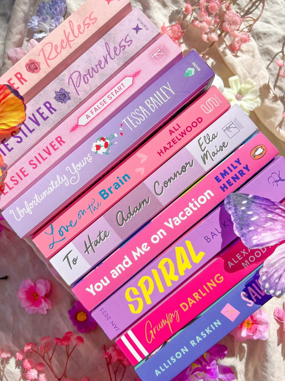 Stack of colorful pink and purple books arranged in a flat lay with flowers around them