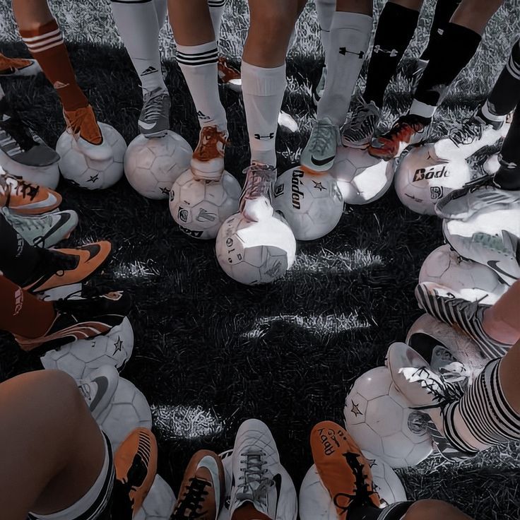 Overhead view of soccer players' legs in circle with soccer balls on grass field