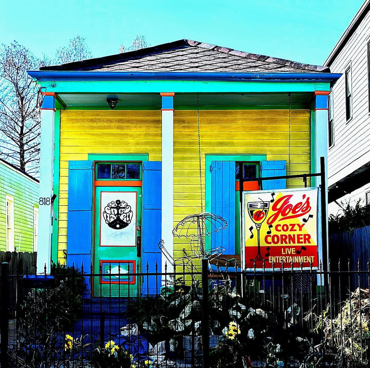 Bright yellow house with blue trim and columns, featuring colorful painted exterior and vintage neon sign
