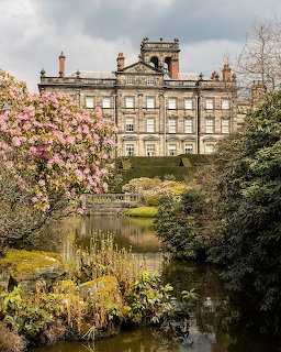 Victorian mansion with ornate chimneys behind garden pond surrounded by pink flowering trees and greenery