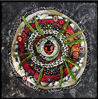 Circular quilt with concentric rings of colorful patterns, insects, leaves, dots, and geometric shapes on dark textured background