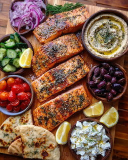 Four grilled salmon fillets with herbs on wooden board surrounded by fresh vegetables and accompaniments