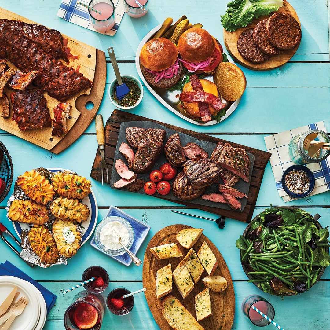 Overhead shot of various grilled meats and vegetables arranged on plates on a blue table