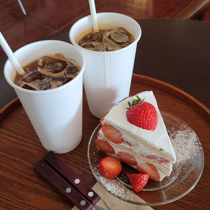 Two iced coffee cups and a slice of strawberry shortcake on a wooden tray