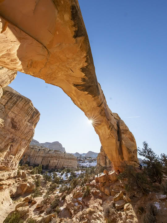Large natural sandstone arch in Southern Utah with blue sky and desert landscape visible through opening