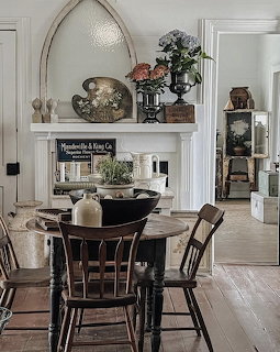 Rustic farmhouse dining room with round wooden table, spindle chairs, and antique-decorated white fireplace mantel