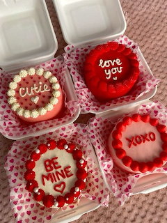 Four heart-shaped Valentine cakes with red and pink icing in small open boxes.