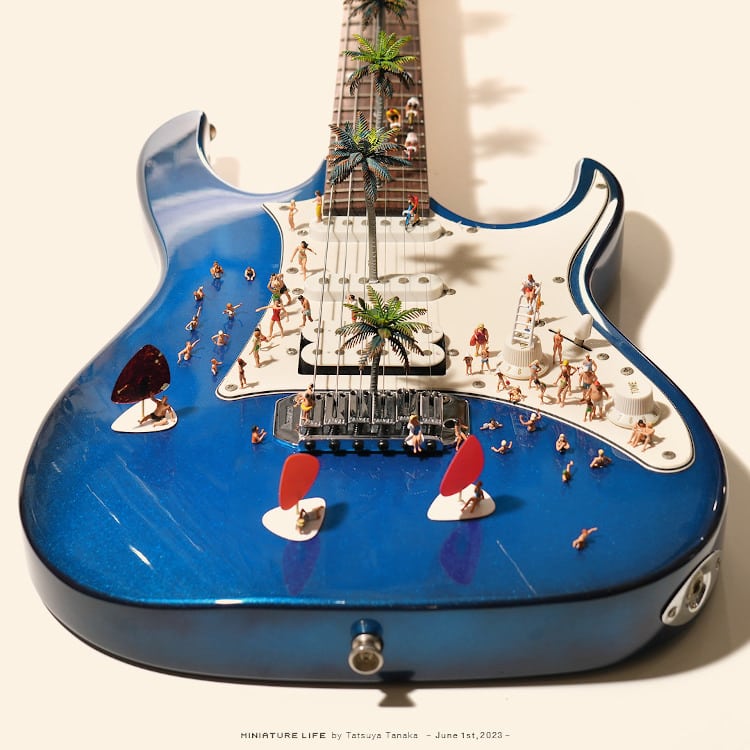 Miniature beach scene diorama constructed inside a blue electric guitar with tiny figures and palm trees