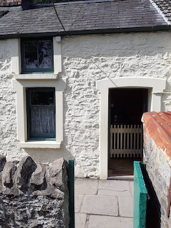 White stone cottage with slate roof, wooden door and window in traditional Welsh style