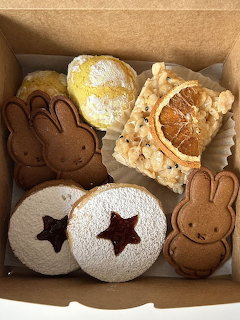 Assorted decorated cookies in a cardboard box including bunny shapes, sandwich cookies, and lemon tart