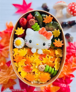 Kawaii bento lunch box with Hello Kitty face made from rice, colorful vegetables, and autumn leaf decorations