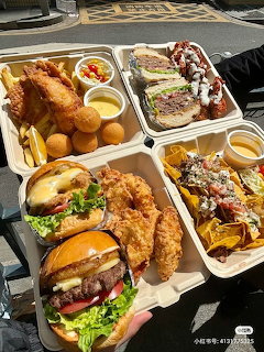 Multiple fast food trays with burgers, fried chicken, tots, waffles and fries on outdoor table