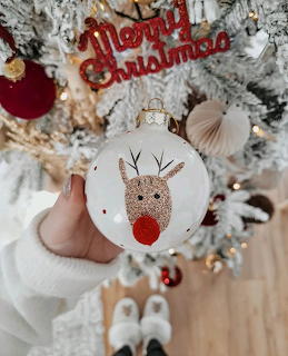 White Christmas ball ornament with Rudolph the red-nosed reindeer illustration hanging on decorated tree
