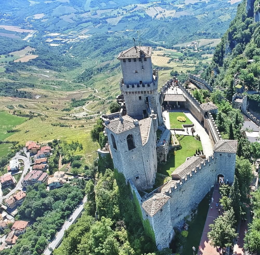 Aerial view of medieval stone castle tower on hilltop in San Marino with green valleys below