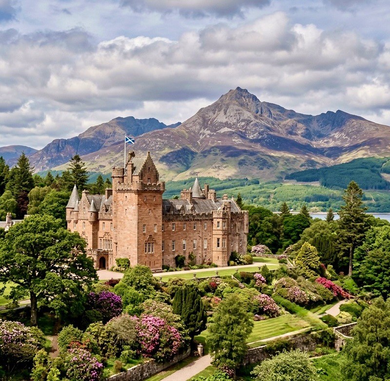 Historic red castle with turrets in gardens with mountains in background