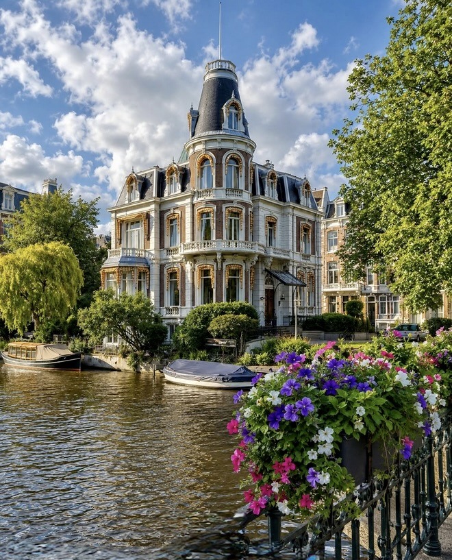 Elegant historic mansion beside an Amsterdam canal with blooming flowers in the foreground