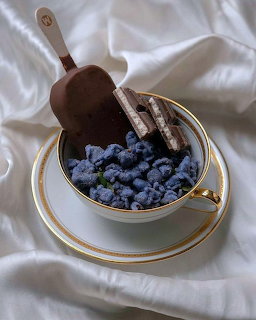 Chocolate popsicle in teacup with blueberries on white satin