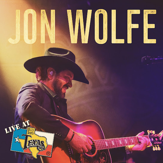Jon Wolfe performing on stage in a cowboy hat, playing an acoustic guitar