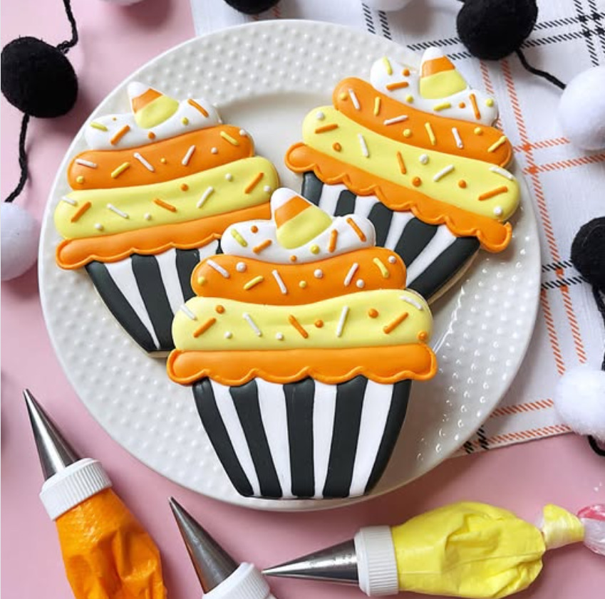 Four decorated cookies shaped like cupcakes with striped bases and orange-yellow icing on a white plate