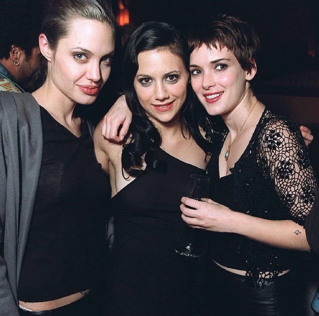 Three women in black outfits posing together at an indoor event