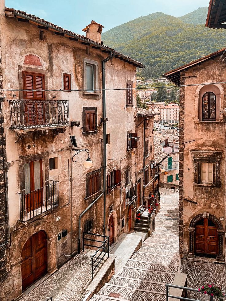 Narrow street between aged buildings in Italian hillside village with mountains behind