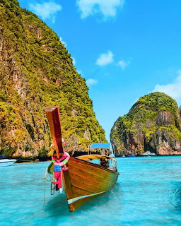 Wooden longtail boat on turquoise water between limestone cliffs and blue sky