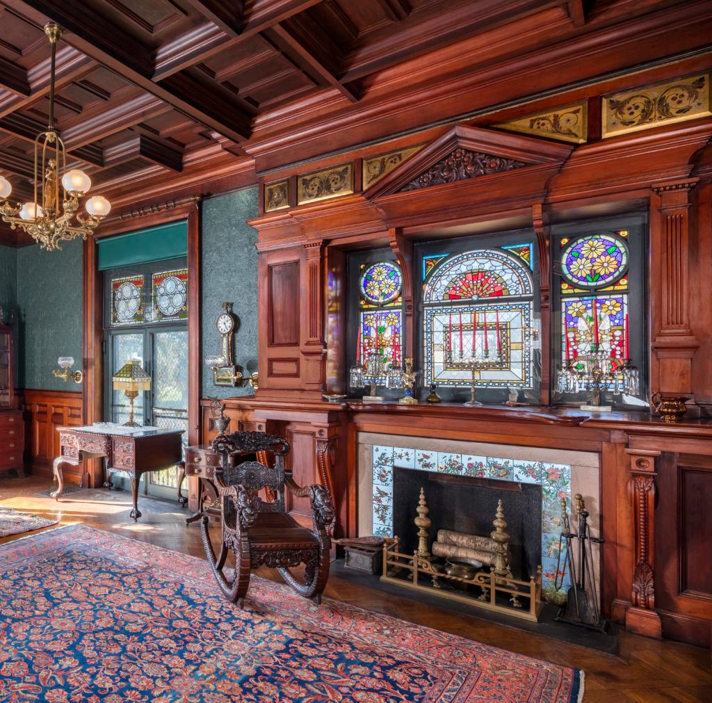 Victorian library with ornate wooden paneling, stained glass windows, fireplace, and antique furniture