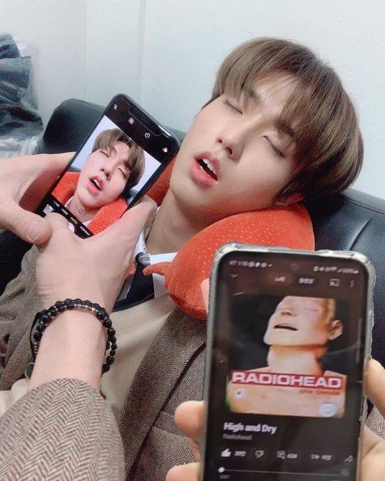 Young man resting with two smartphones held nearby, one showing a selfie and one a Radiohead music app