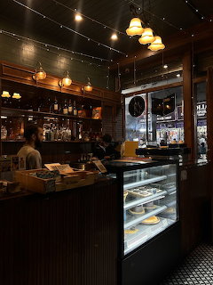 Dark cozy cafe interior with bar counter, pastry display case, warm lighting and wooden shelves