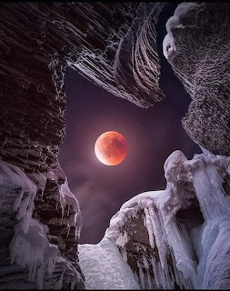 Blood moon seen through icy rocky canyon walls against a purple starry night sky