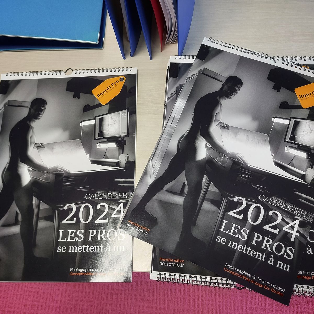 2025 wall calendar showing artistic silhouette photo, lying on red desk with office supplies