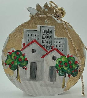 Hand-painted wooden ornament with village houses, red roofs, green trees, and buildings on gold background