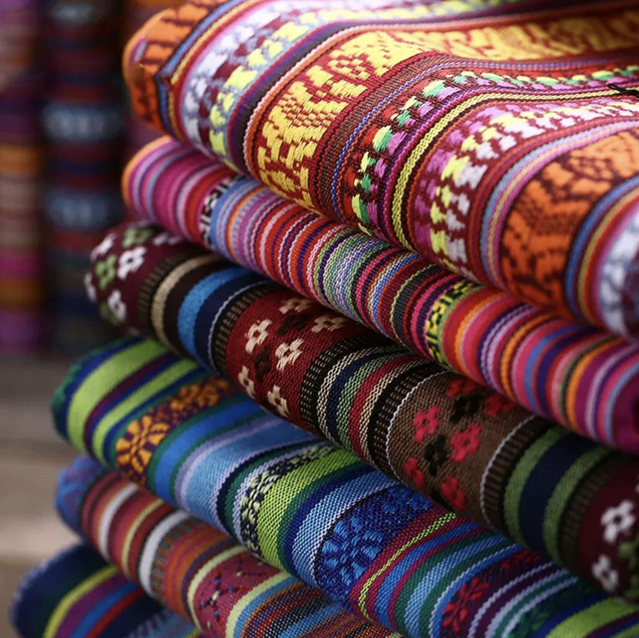 Close-up of stacked colorful woven fabrics with striped and geometric patterns