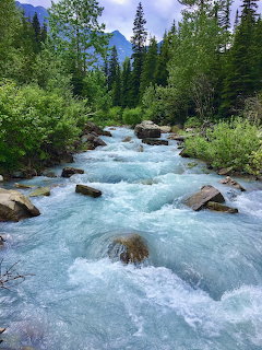 Rushing mountain stream in a pine forest with rocks and distant blue peaks