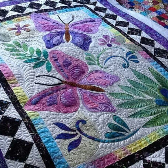 Handmade quilt with purple, pink, and blue butterflies, green ferns, and black-and-white checkered border