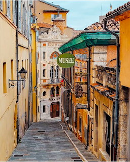 Narrow coblestone street in Grasse, France with colorful old buildings and a Musee sign
