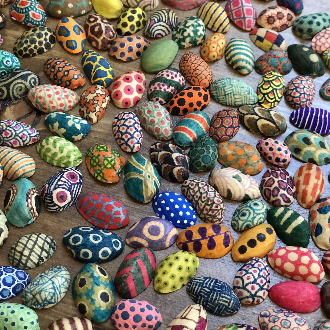 Dozens of small seashells painted with vibrant patterns including dots, stripes, zigzags and geometric designs