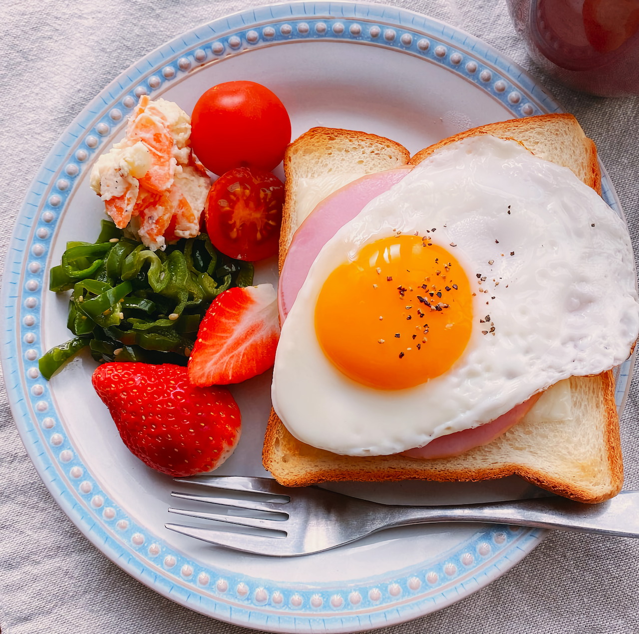 Breakfast plate with sunny-side-up egg on toast, strawberries, tomatoes, spinach, and shrimp