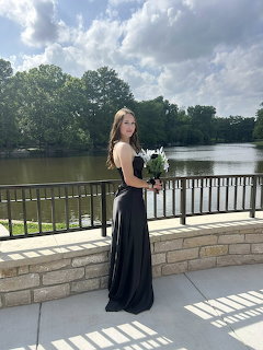 Woman in elegant black dress holding white flowers by lakeside terrace