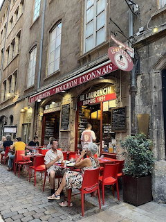 French bistro with red chairs on cobblestone street, diners seated at outdoor tables in Lyon